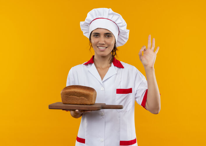切面带微笑的年轻女厨师穿着厨师制服 拿着面包放在砧板上 并用复印空间显示出良好的姿势制服板子拿着