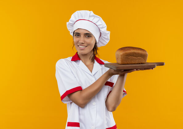 制服面带微笑的年轻女厨师穿着厨师制服拿着面包放在有复印空间的砧板上厨师切着穿着