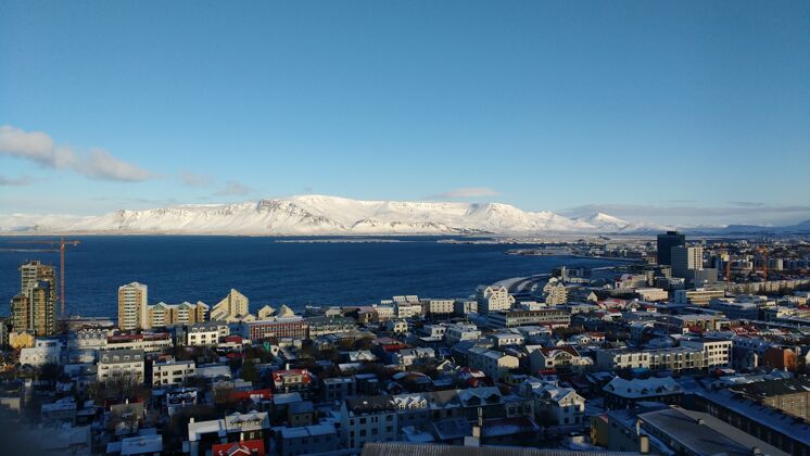 航空空中拍摄的沿海城市雷克雅未克与白雪覆盖的山脉对蓝天海岸云冰岛
