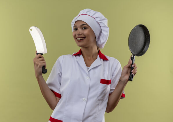 切肉刀微笑的年轻厨师女身穿厨师制服手持菜刀和煎锅厨师煎炸佩带