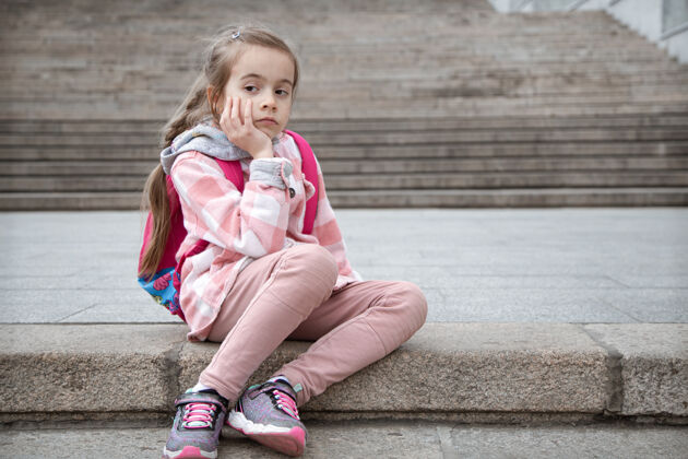 孩子一个悲伤的小女孩背着公文包坐在楼梯上的画像回学校去懒惰小学生台阶