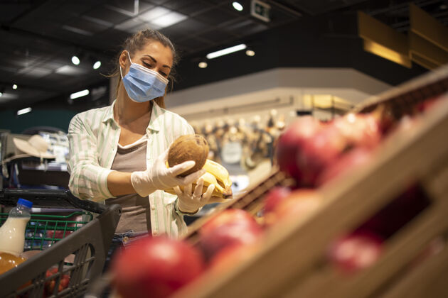 购买戴着卫生口罩 橡胶手套和购物车的妇女在杂货店购买日冕病毒期间的水果 准备进行大流行隔离商店保健传染性