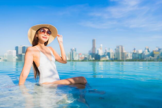 天际线美丽的亚洲年轻女子在户外游泳池周围放松 城市景色尽收眼底身体高度假村