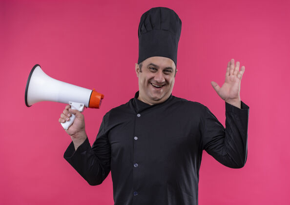 男身着厨师制服的快乐中年男厨师手举喇叭 站在孤立的粉红色墙上提高厨师喇叭