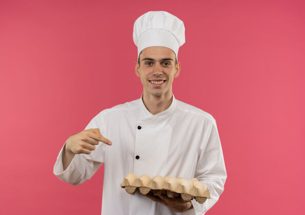 批面带微笑的年轻男厨师身穿厨师制服 指着一批鸡蛋男手指穿