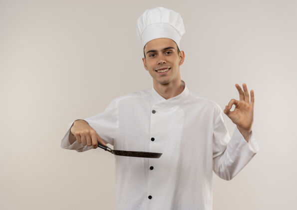 厨师面带微笑的年轻男厨师身穿厨师制服 手拿煎锅 摆出很好的姿势制服展示好的