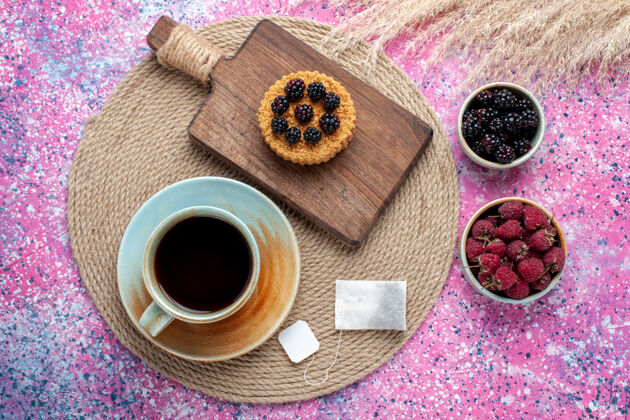 杯子顶视图的小蛋糕与不同的浆果和茶杯在粉红色的表面生脸粉水果