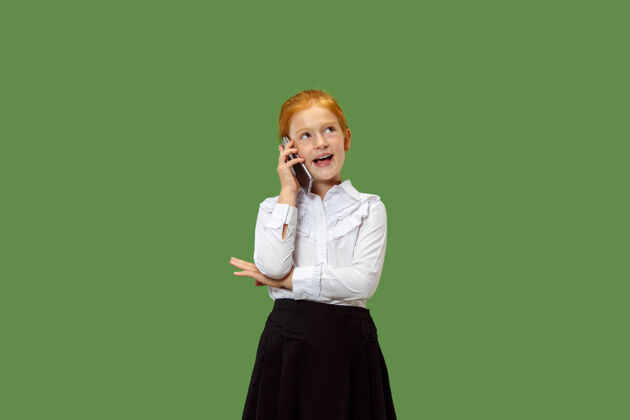 教育快乐的少女站着 微笑着用手机在时尚的绿色工作室背景上美丽的女性半身像人类的情感 面部表情的概念电话女性年轻
