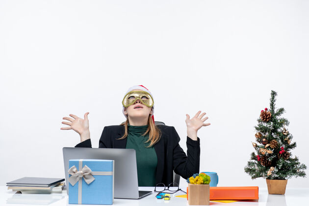 圣诞节圣诞气氛与年轻女子戴着圣诞老人的帽子 戴着面具坐在一张桌子上看上面的白色背景工作圣诞老人年轻