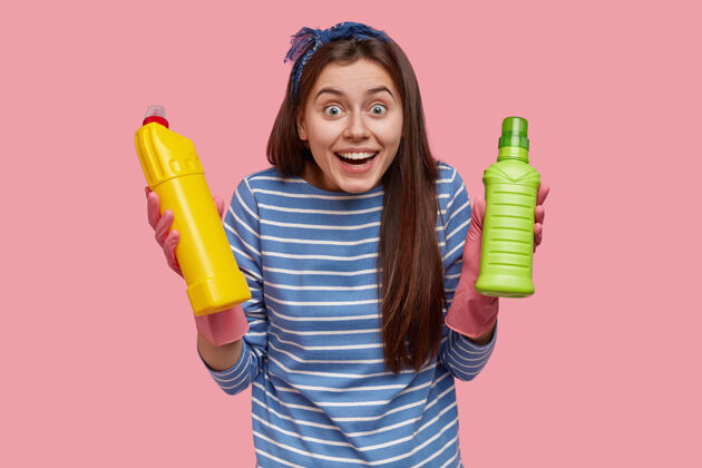手套快乐的欧洲女人的上身镜头 表情欢快 穿着条纹衣服 拿着装有清洁用品的瓶子瓶子服务产品