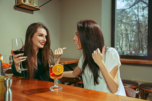 友谊女朋友在酒吧喝酒她们坐在一张有鸡尾酒的木桌旁酒酒杯交谈