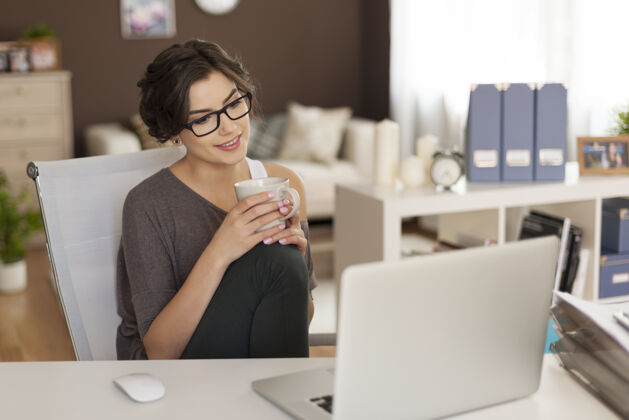 家庭室内在家喝咖啡时看着笔记本电脑的漂亮女人室内工作咖啡杯