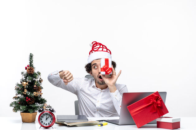 帽子圣诞节心情惊讶的商人与圣诞老人的帽子提高他的礼物 他的脸上 检查他的tme白色背景圣诞老人礼物提高