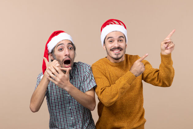 查看前视图两个戴着圣诞帽的男人一个在展示什么 另一个在孤立的背景上打电话给我呼叫帽子成人