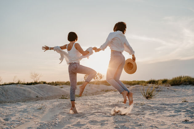 在一起快乐的两个年轻女子在日落海滩上玩得开心 男女同性恋的爱情浪漫爱伴侣夫妇