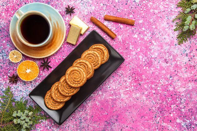 甜点顶视图中的甜饼干与肉桂和茶在浅粉红色的表面黑色形式饼干里面蛋糕