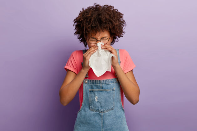 牛仔布卷曲的年轻女性感到不适 用白色组织擤鼻子 流鼻涕 感冒症状或过敏疾病病人过敏
