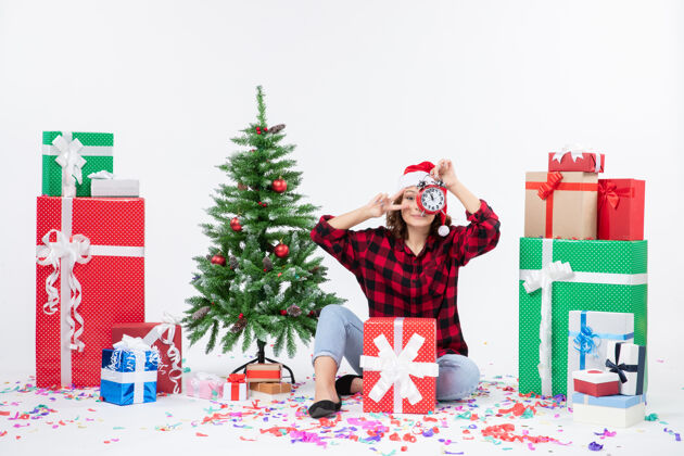 人前视图的年轻女子坐在圣诞礼物周围拿着白色墙上的时钟抱着庆祝微笑