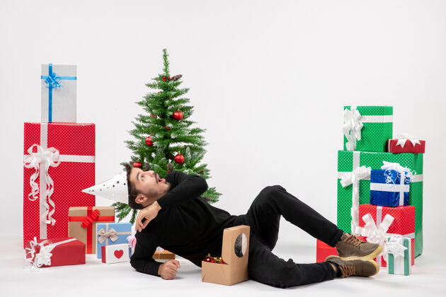 庆祝年轻人坐在白色墙上的节日礼物周围的正面视图圣诞节模型圣诞快乐