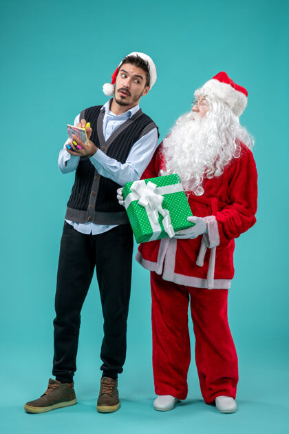 圣诞老人前视图：圣诞老人和正在蓝色背景上做笔记的年轻男性蓝色圣诞老人男性