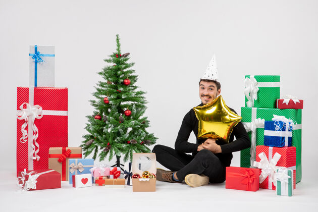 礼物年轻人围坐在礼物旁边 拿着金星在白墙上人前面圣诞