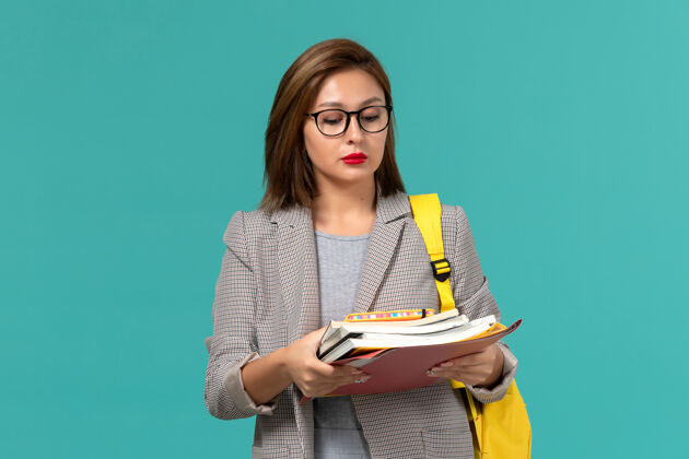 人身着灰色夹克 黄色背包 蓝色墙壁上拿着书的女学生正面图正面学生成人