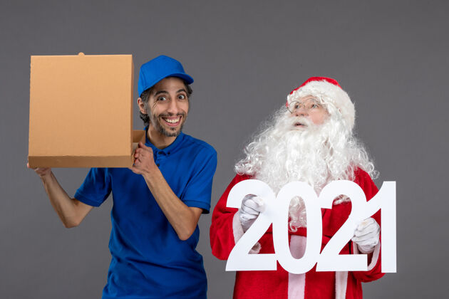 人圣诞老人的正面图 男信使拿着购物袋和食品盒在灰色的墙上帽子圣诞老人圣诞