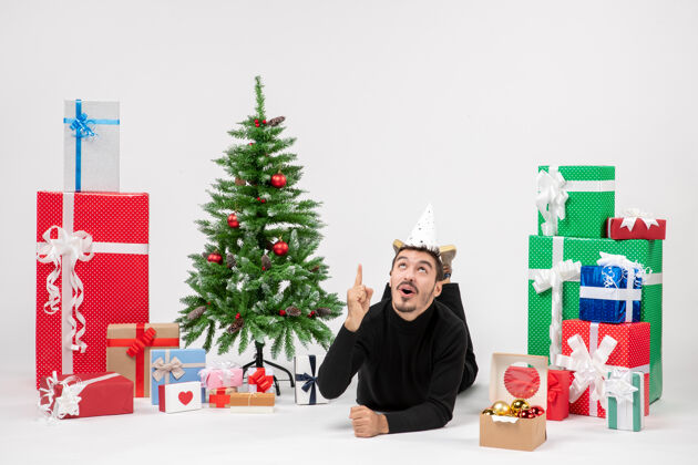 圣诞快乐年轻人躺在白色墙上的节日礼物周围的正面视图礼物人人