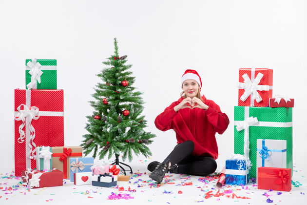 季节年轻女子坐在白色墙壁上的节日礼物周围的正面视图装饰庆祝圣诞快乐