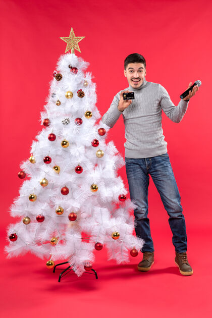 微笑圣诞气氛 情绪激动的家伙站在装饰好的圣诞树旁 拿着麦克风和电话讲话电话快乐站着