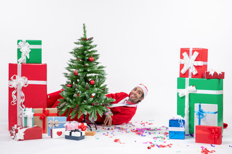 说谎圣诞老人躺在圣诞树后面 白色背景上的礼物旁 节日气氛热烈圣诞树圣诞老人季节