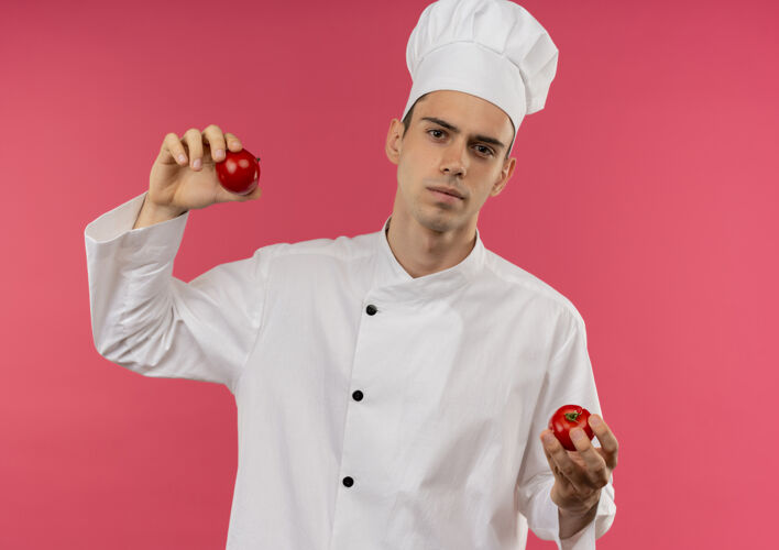 厨师年轻的男厨师穿着厨师制服 拿着西红柿站在孤立的粉红色墙上拿着男性戴着