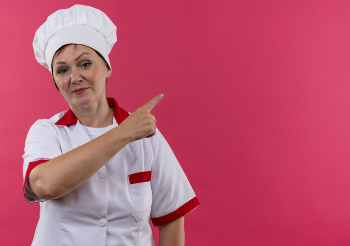手指身着厨师制服的中年女厨师用手指向一侧指着隔离的粉色墙壁 并留有复印空间高兴厨师制服