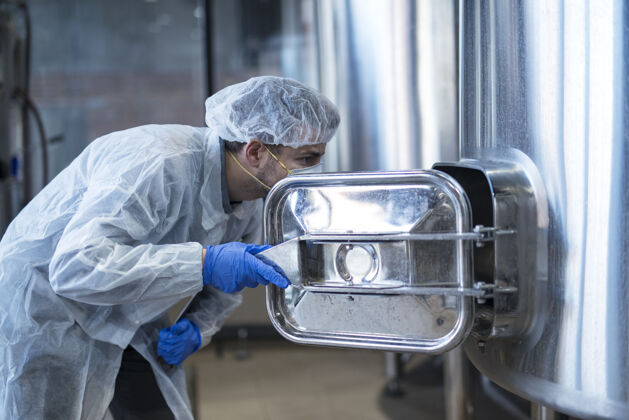 西装穿着白西装的技术员在食品厂生产线上查看机器内部保持质量工作