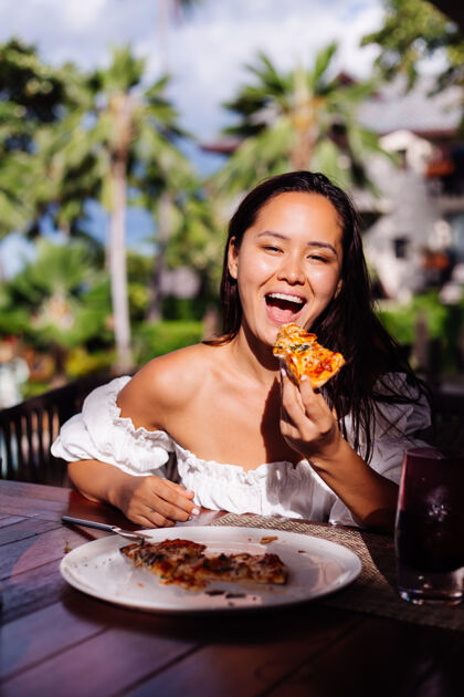 欢快快乐的亚洲美女在阳光明媚的日子里饿着肚子吃披萨在户外餐厅日落的阳光下女人在享受美食在午餐的乐趣意大利语奢华放松