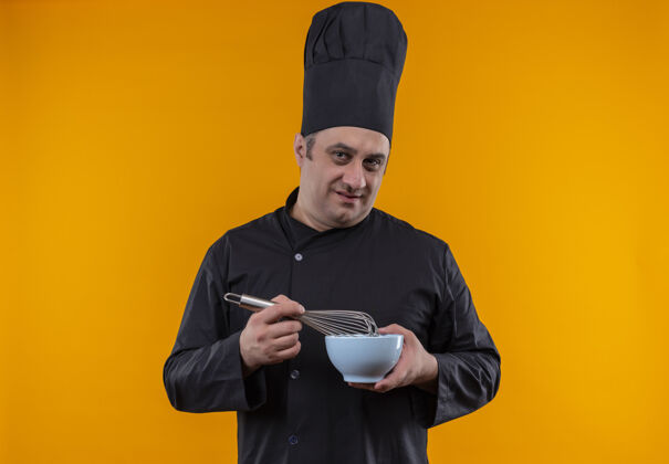 厨师身穿厨师制服的中年男厨师 手拿搅拌器和碗 站在黄色的墙上碗中年制服