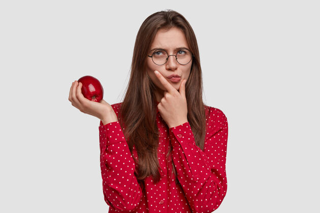 体重严肃体贴的美女照片托着下巴 扛着苹果 有沉思的表情 穿着红衬衫个人营养女士