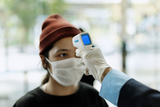 体温计戴着医用面罩的女人用电子温度计测量体温传播测量手套