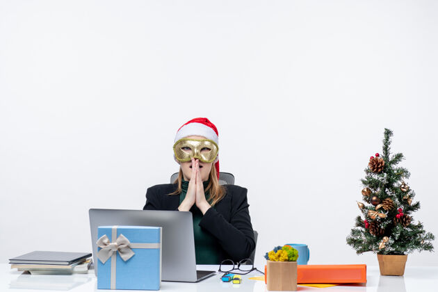 电脑圣诞气氛与紧张的年轻女子戴着圣诞老人的帽子和面具坐在一张白色背景的桌子上专业年轻笔记本电脑