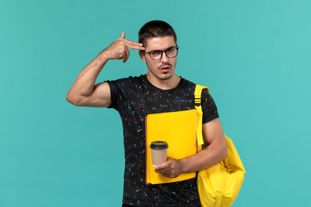 学生前视图中的男学生穿着深色t恤黄色背包 蓝色墙上放着不同的文件和咖啡男大学不同