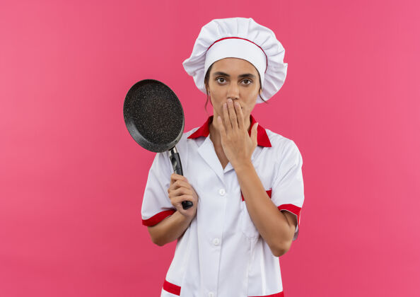 拿着惊讶的年轻女厨师穿着厨师制服拿着煎锅 用手捂着嘴 留着复印空间穿嘴女