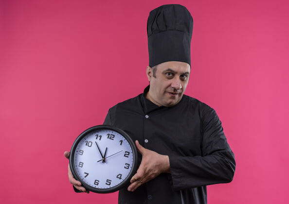 制服穿着厨师制服的中年男厨师 拿着挂钟站在粉红色的墙上 墙上留有复制空间厨师厨师钟