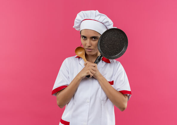 厨师年轻的女厨师穿着厨师制服 拿着勺子和煎锅 放在隔离的粉红色墙上 有复印空间女拿着穿