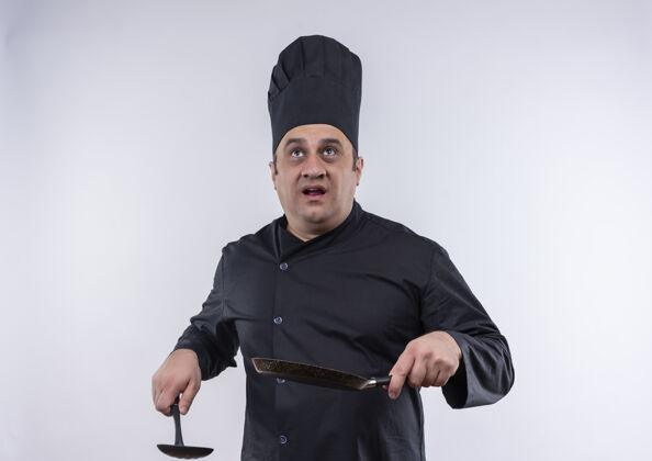 男看着一个身穿厨师制服的中年男厨师 手里拿着煎锅和抹刀 站在隔离的白色墙上拿着看着抹刀