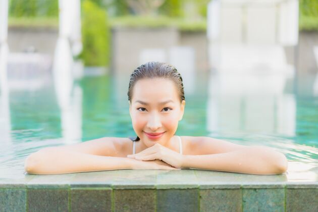 泳装肖像美丽的亚洲年轻女子放松微笑周围的室外游泳池在酒店度假村性感健康日光浴
