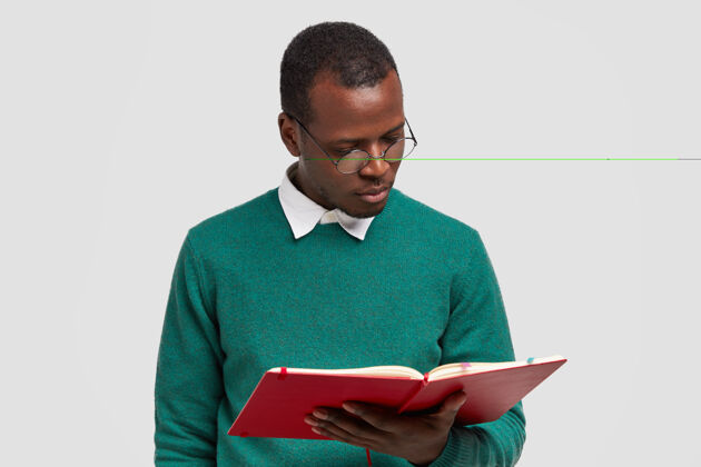 非洲严肃专注的黑皮肤年轻人的照片集中在课本上 戴着圆眼镜 穿着绿色毛衣 在大学学习教科书姿势学习