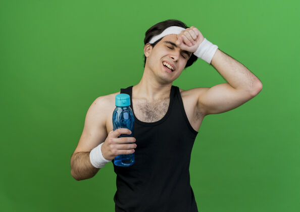 站着一个穿着运动服 戴着头巾 拿着一瓶水的年轻人看起来很累穿着看着运动