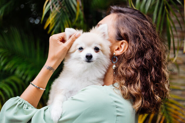 绿色欧洲棕褐色卷曲女人的户外肖像抱着快乐的宠物狗波美拉尼亚斯皮茨肖像毛茸茸的纯种
