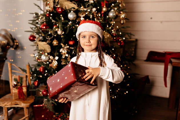 季节圣诞节的时候 快乐的孩子戴着圣诞帽 拿着圣诞礼物在圣诞树上摆姿势室内礼物装饰