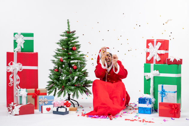 年轻圣诞气氛与年轻害怕圣诞老人坐在圣诞树和礼物在白色背景上不同的颜色圣诞老人坐着不同